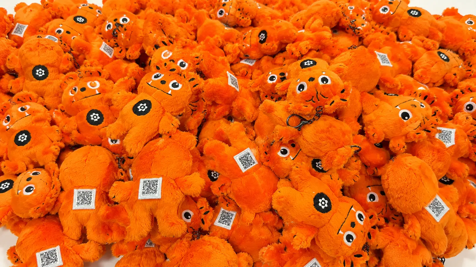 Hundreds of custom-made orange character plush keyrings piled up with QR tags